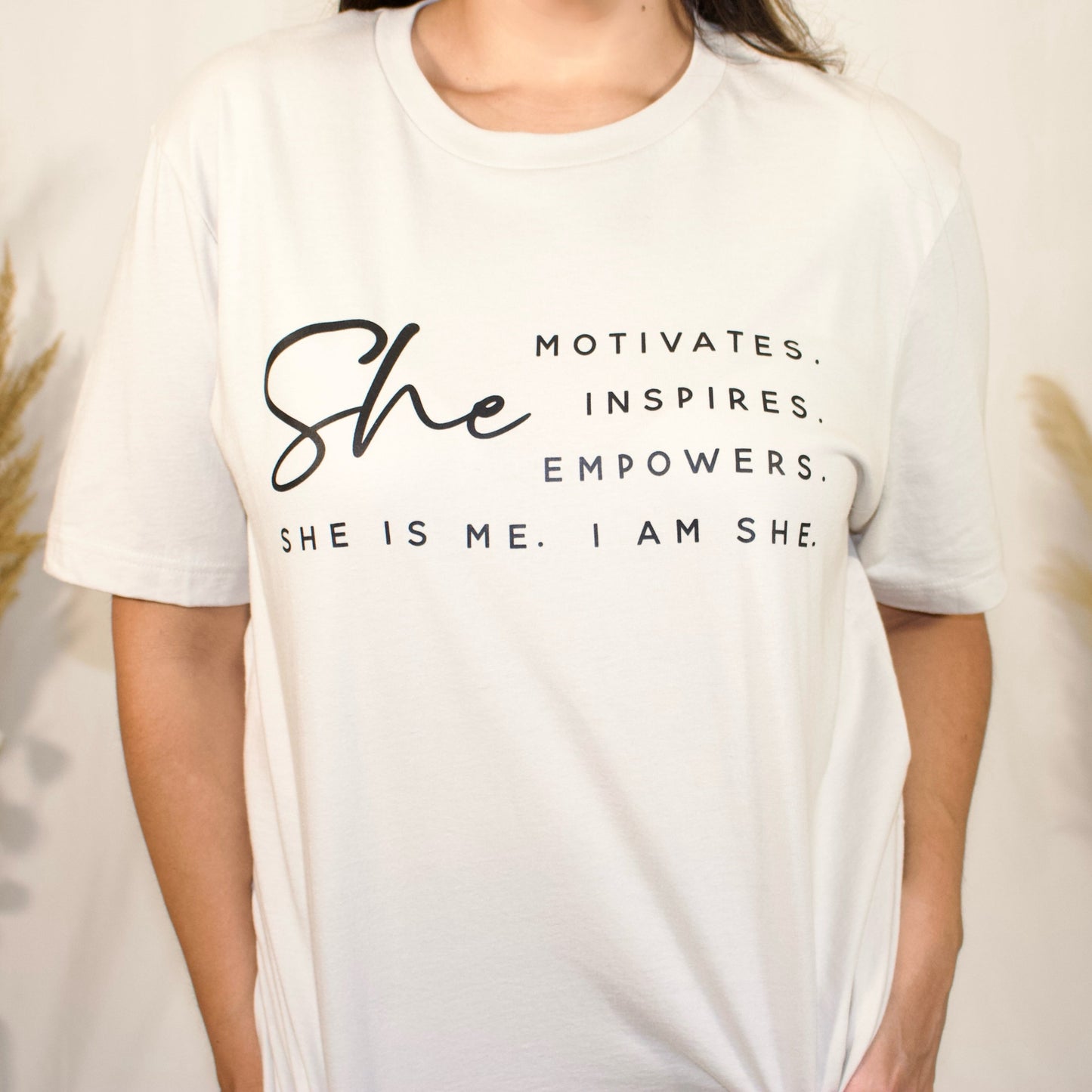 front side, close up of a t-shirt with wording saying She motivated, inspires, empowers, she is me, i am she in t-shirt color white