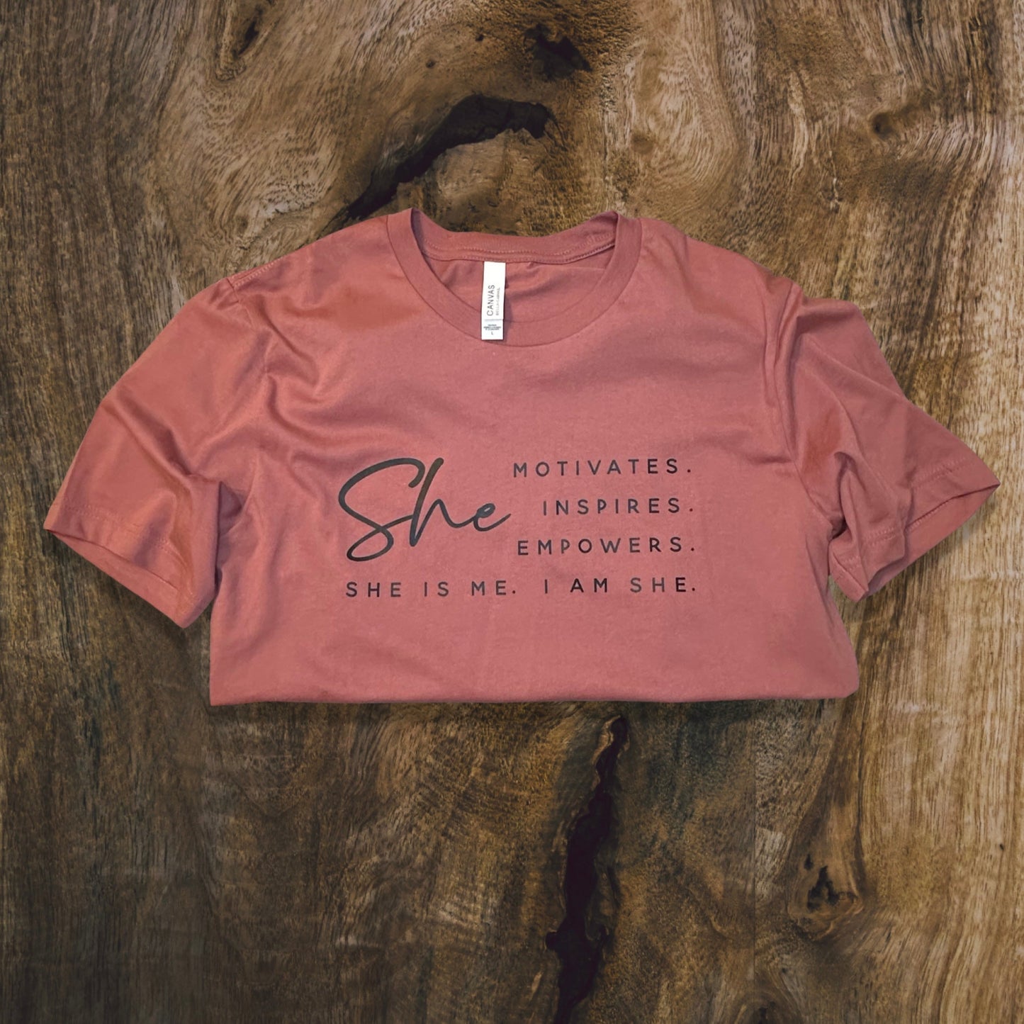 front side, close up of a t-shirt with wording saying She motivated, inspires, empowers, she is me, i am she in t-shirt color mauve