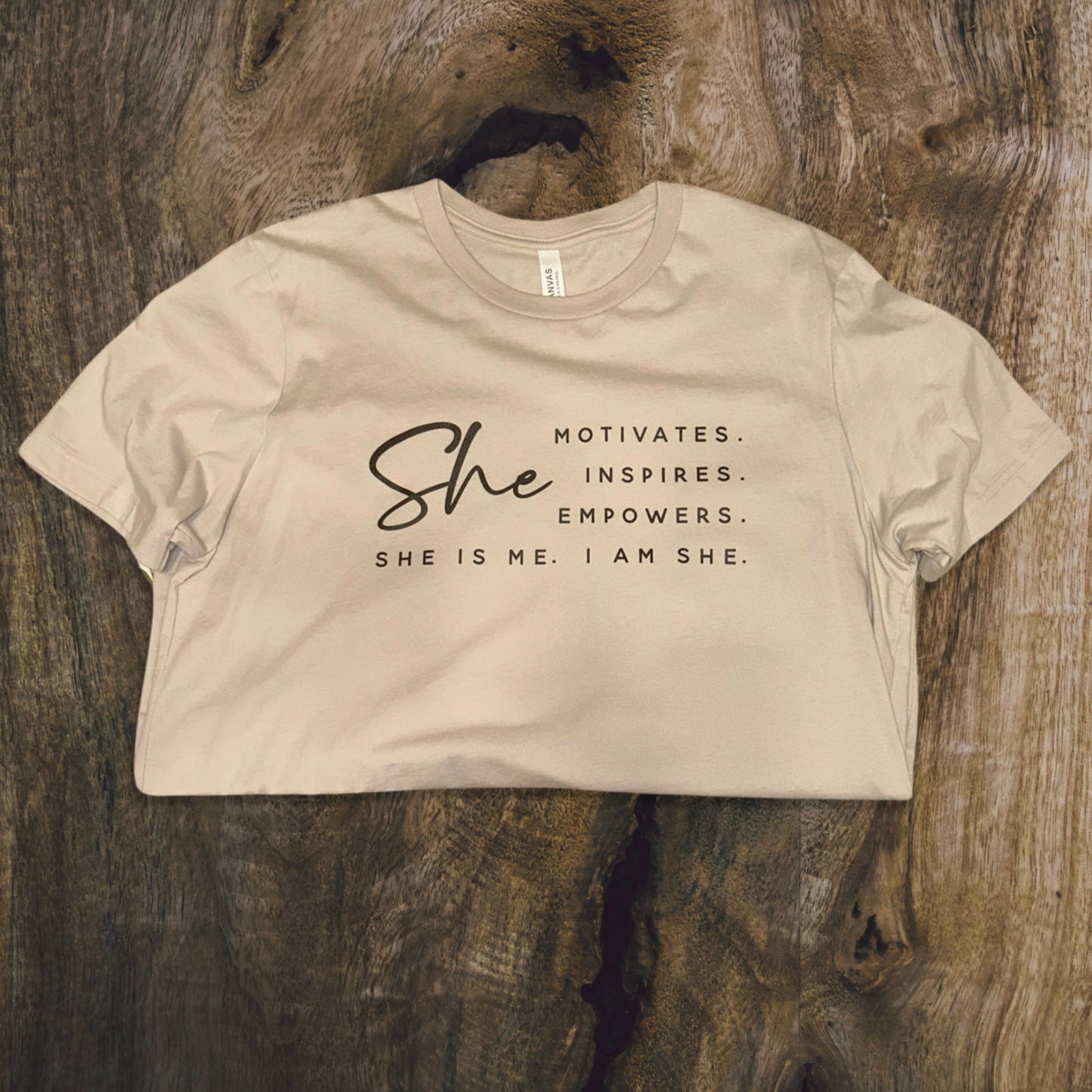 front side, close up of a t-shirt with wording saying She motivated, inspires, empowers, she is me, i am she in t-shirt color tan