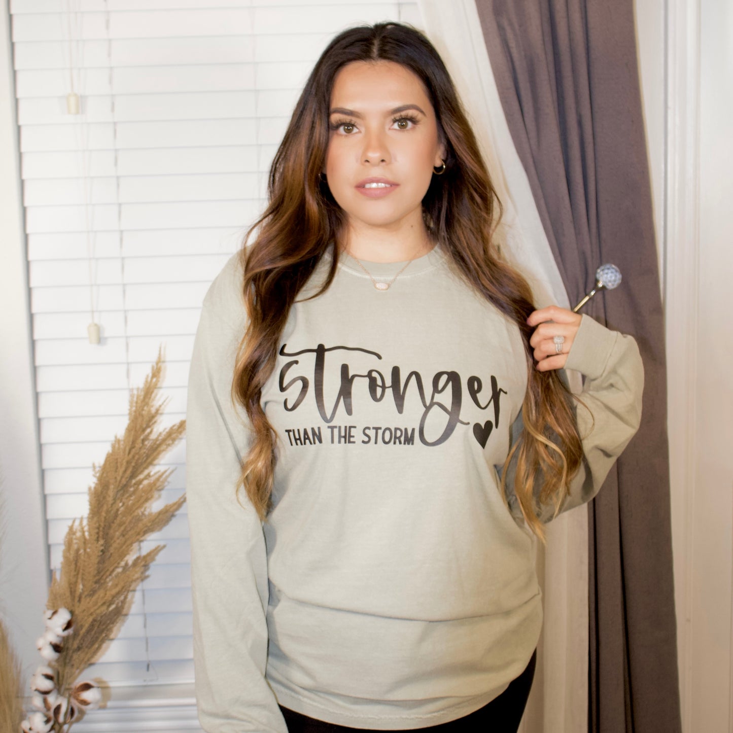 black letters with stronger than the storm with a sandstone long sleeve t-shirt