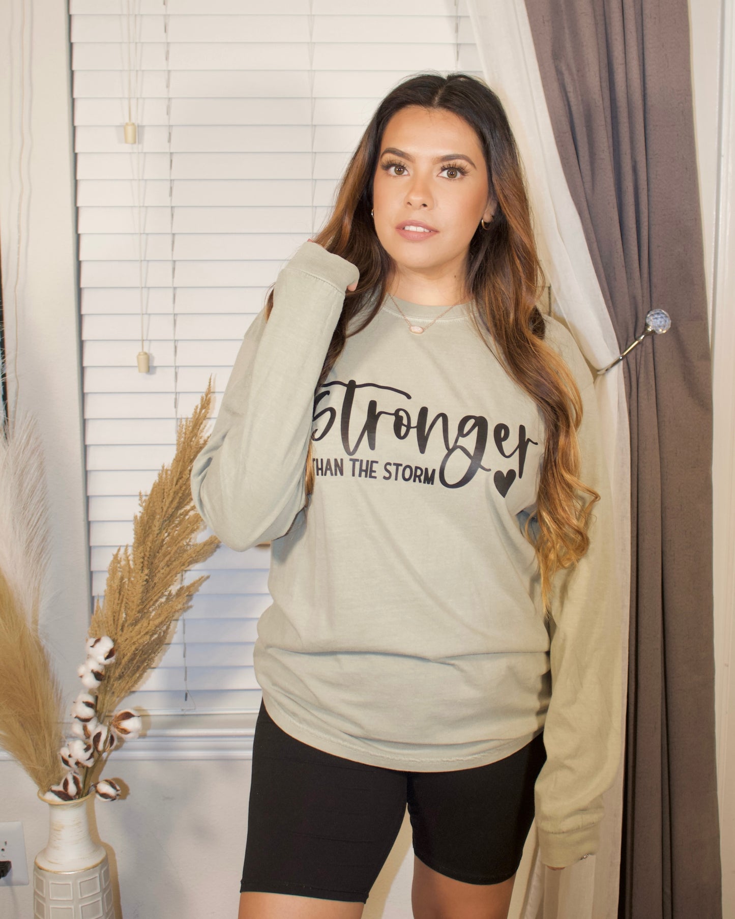 black letters with stronger than the storm with a sandstone long sleeve t-shirt