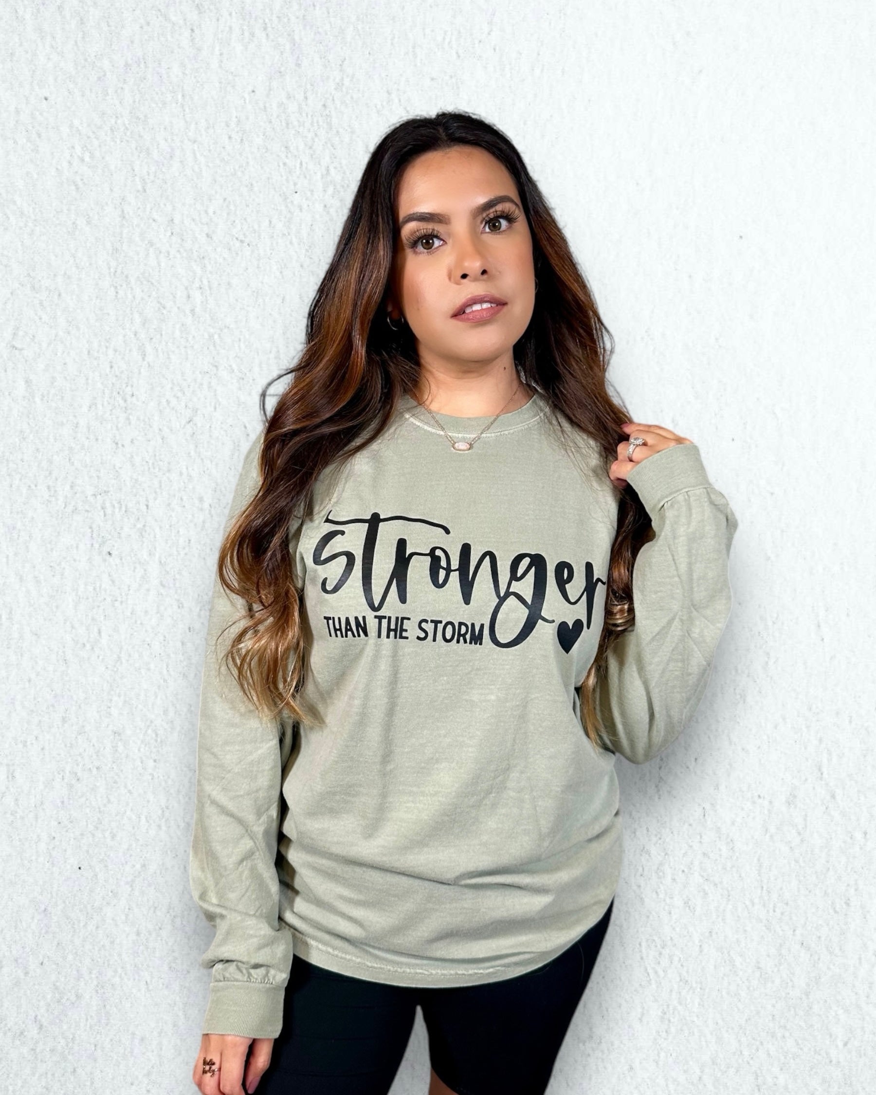 black letters with stronger than the storm with a sandstone long sleeve t-shirt