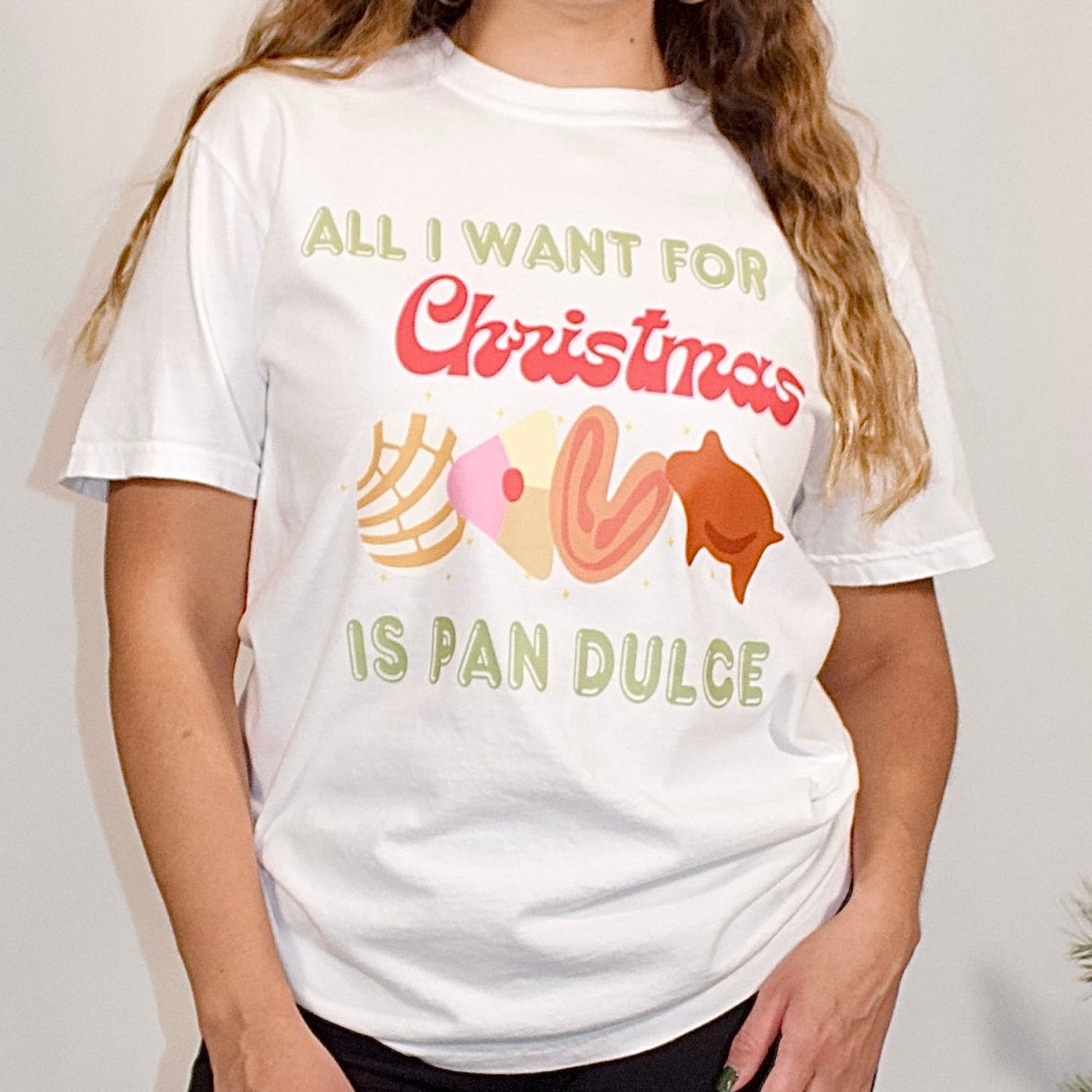 WHITE T SHIRT FRONT SIDE CLOSE UP WITH COLORFUL LETTERS THAT SAYS ALL I WANT FOR CHRISTMAS IS PAN DULCE