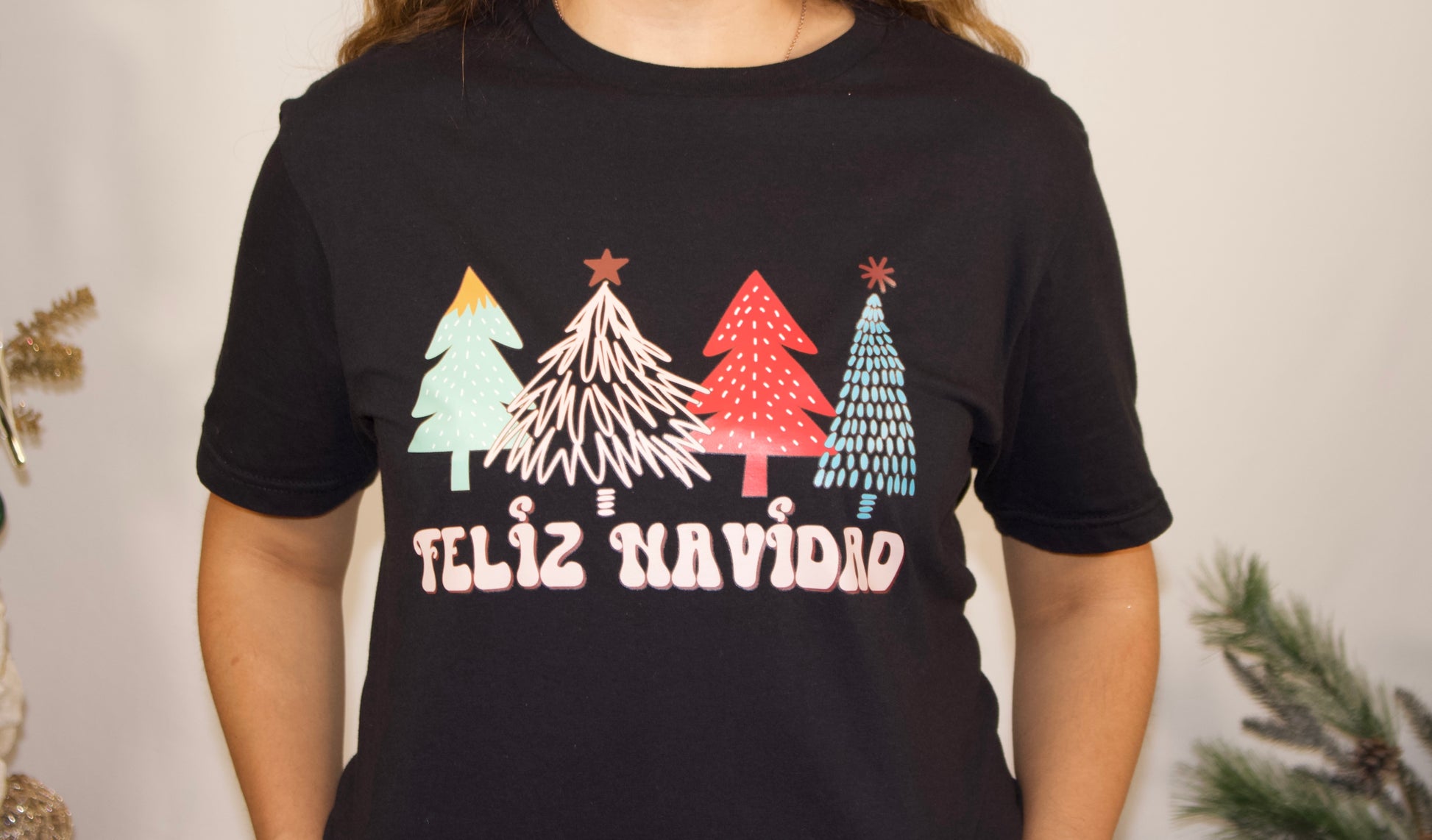 BLACK TSHIRT FRONT SIDE CLOSE UP WITH COLORFUL CHRISTMAS TRESS AND WITH FELIZ NAVIDAD PINK LETTERS